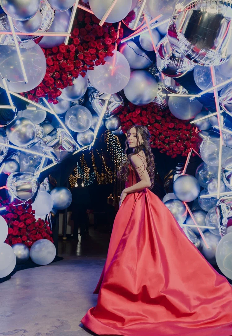 Chica bajo un arco de rosas rojas, globos plateados y luces led