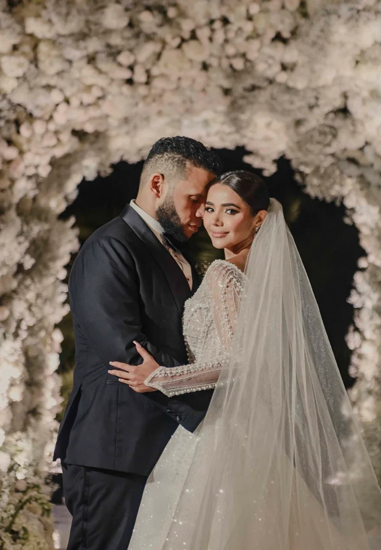 Pareja abrazada bajo un arco de flores blancas para bodas