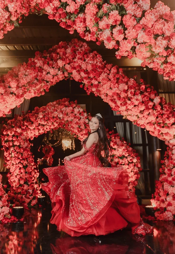 Recuerdo eterno de chica posando frente a arcos de flores rojas